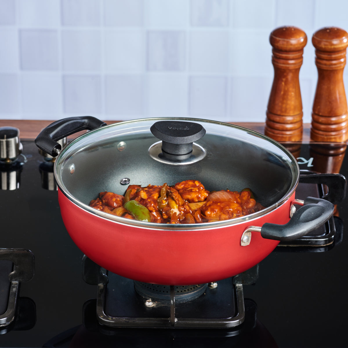 Red nonstick kadai with glass lid cooking vegetables on a gas stove, ideal for everyday Indian cooking.