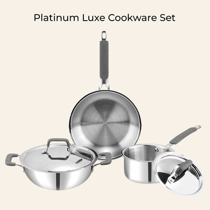 Set of platinum luxe cookware including a frying pan, saucepan, and pot on a beige background.