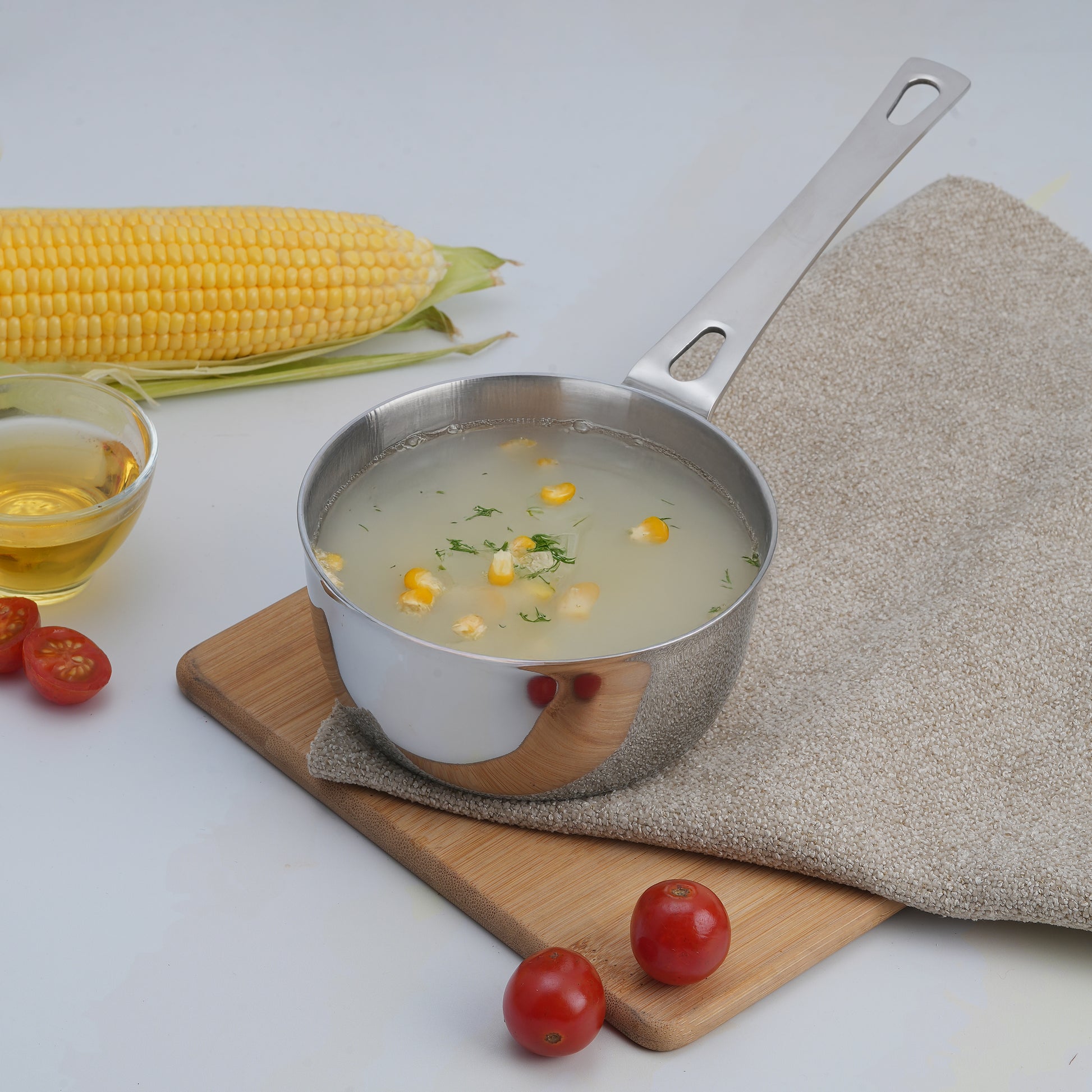 Metal pot of soup with corn and tomatoes on a wooden board