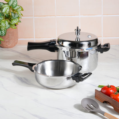 A silver-colored Vinod Cookware pressure cooker with a deep pan and lid placed on a kitchen counter, with tomatoes and a cooking spoon in the foreground.