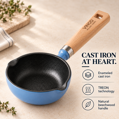 A blue and black cast iron saucepan with a natural wood handle, shown on a beige surface with decorative herbs and text highlighting product features.