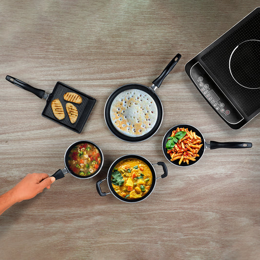 An overhead image of a 5 piece mini cookware set by Vinod Cookware, displaying a variety of pots and pans on a wooden surface with a gas stove in the background.
